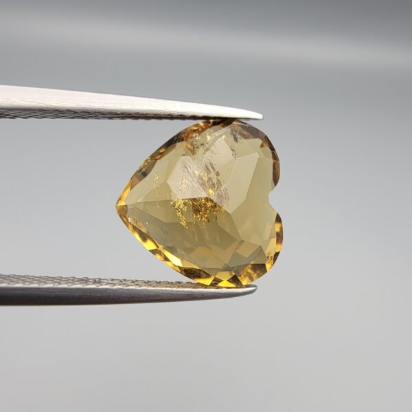 Studio close-up photographs showing the high-brilliance facet pattern, romantic heart outline, luminous golden body, and striking sparkling untreated internal crystal inclusions of a 5.68 carat heart shape natural citrine quartz loose gemstone held in precision tweezers.