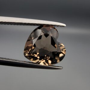 Studio close-up photographs showing the precision facet pattern, premium clarity, and rich brown color of a 3.29 carat heart shape brilliant cut natural smoky quartz loose gemstone held securely in tweezers.