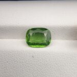 ​Close-up top-down view of a 2.39 carat cushion-shaped natural vivid green tourmaline loose gemstone resting against a white textured background, showcasing its rich color and characteristic internal inclusions.