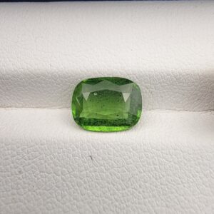 ​Close-up top-down view of a 2.39 carat cushion-shaped natural vivid green tourmaline loose gemstone resting against a white textured background, showcasing its rich color and characteristic internal inclusions.
