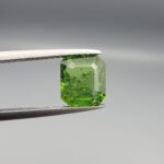 Studio close-up photograph showcasing the top-down view of an octagonal step-cut 2.19 carat natural vivid green tourmaline loose gemstone held securely in precision tweezers.