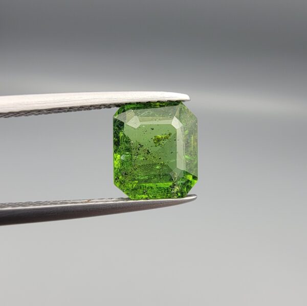 Studio close-up photograph showcasing the top-down view of an octagonal step-cut 2.19 carat natural vivid green tourmaline loose gemstone held securely in precision tweezers.
