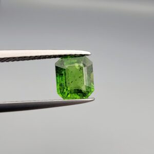 Studio close-up photograph showcasing the top-down view of an octagonal step-cut 1.39 carat natural vivid green tourmaline loose gemstone held securely in precision tweezers.