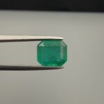 Studio close-up photograph showcasing an octagonal step-cut 2.10 carat natural green emerald gemstone held securely in precision tweezers.