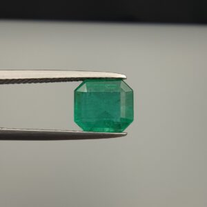 Studio close-up photograph showcasing an octagonal step-cut 2.10 carat natural green emerald gemstone held securely in precision tweezers.
