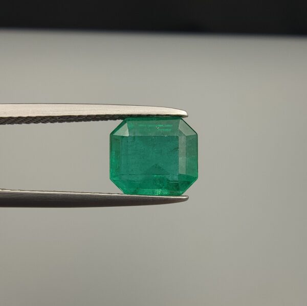 Studio close-up photograph showcasing an octagonal step-cut 2.10 carat natural green emerald gemstone held securely in precision tweezers.