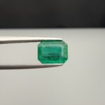 Studio close-up photograph showcasing an octagonal step-cut 1.97 carat natural green emerald gemstone held securely in precision tweezers.