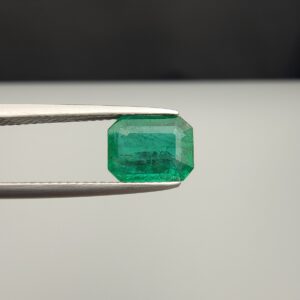 Studio close-up photograph showcasing an octagonal step-cut 1.97 carat natural green emerald gemstone held securely in precision tweezers.