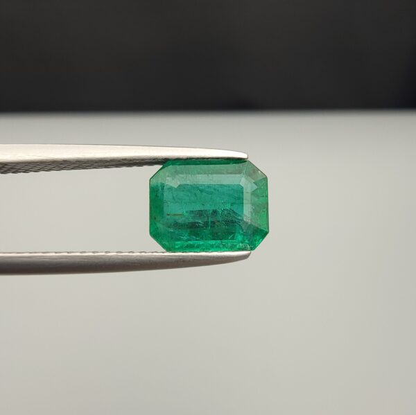 Studio close-up photograph showcasing an octagonal step-cut 1.97 carat natural green emerald gemstone held securely in precision tweezers.