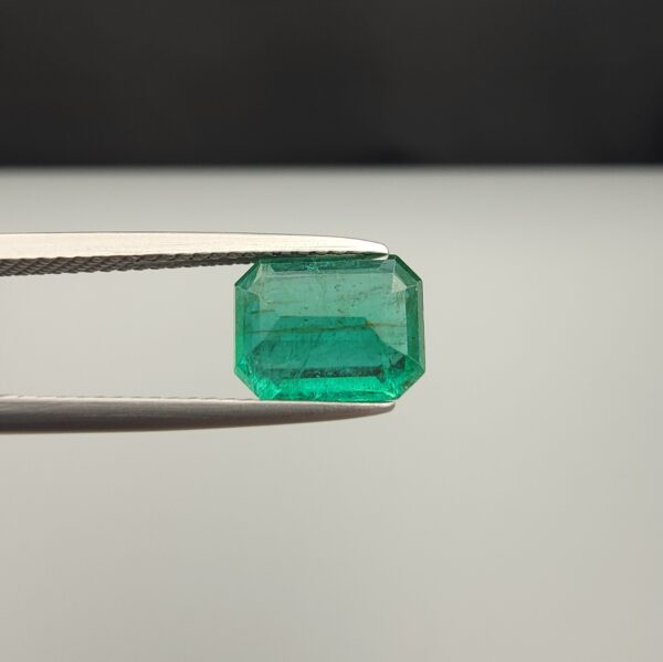 Studio close-up photograph showcasing an octagonal step-cut 1.97 carat natural green emerald gemstone held securely in precision tweezers.