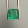 Studio close-up photograph showcasing a cushion-cut 2.12 carat natural green emerald gemstone held securely in precision tweezers, revealing distinctive internal black silk inclusions.