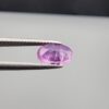 Studio close-up photograph showcasing a 1.55-carat oval-cut natural vivid purple sapphire loose gemstone featuring visible internal feathering and a subtle flash of blue zoning near the lower girdle edge, held securely in precision tweezers.