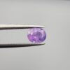 Studio close-up photographs showcasing a 1.44-carat oval-cut natural vivid purple sapphire loose gemstone with visible internal feathering and distinct color zoning, held securely in precision tweezers against a neutral grey background.