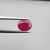 Studio close-up photographs showcasing a 2.16-carat oval-cut premium quality natural unheated ruby loose gemstone held securely in precision tweezers against a neutral grey background.