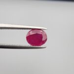 Studio close-up photographs showcasing a 2.16-carat oval-cut premium quality natural unheated ruby loose gemstone held securely in precision tweezers against a neutral grey background.