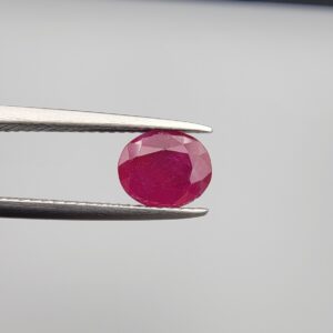 Studio close-up photographs showcasing a 2.16-carat oval-cut premium quality natural unheated ruby loose gemstone held securely in precision tweezers against a neutral grey background.