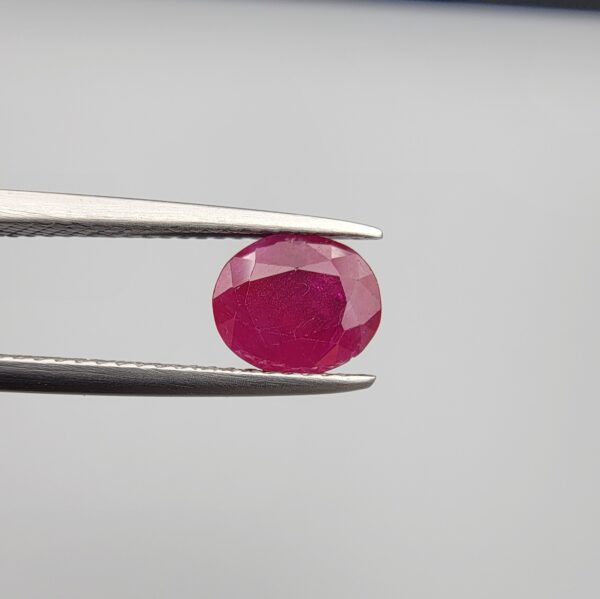 Studio close-up photographs showcasing a 2.16-carat oval-cut premium quality natural unheated ruby loose gemstone held securely in precision tweezers against a neutral grey background.