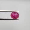 Studio close-up photographs showcasing a 2.16-carat oval-cut premium quality natural unheated ruby loose gemstone held securely in precision tweezers against a neutral grey background.