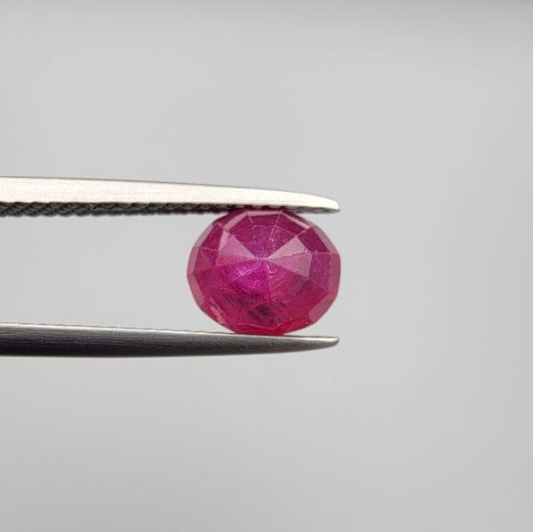 Studio close-up photographs showcasing a 2.16-carat oval-cut premium quality natural unheated ruby loose gemstone held securely in precision tweezers against a neutral grey background.
