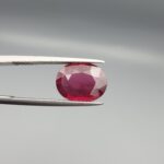Studio close-up photographs displaying a 4.27-carat oval-cut natural rhodolite garnet gemstone held securely in precision tweezers against a neutral grey background.