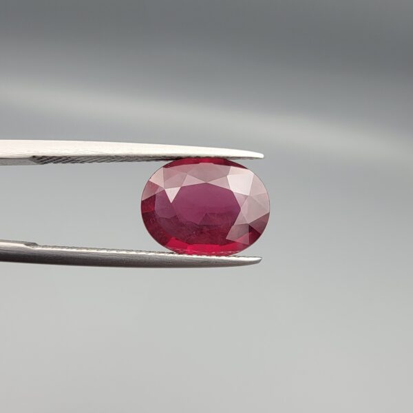 Studio close-up photographs displaying a 4.27-carat oval-cut natural rhodolite garnet gemstone held securely in precision tweezers against a neutral grey background.