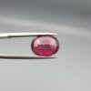 Studio close-up photographs displaying a 4.27-carat oval-cut natural rhodolite garnet gemstone held securely in precision tweezers against a neutral grey background.
