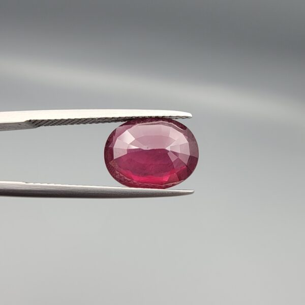 Studio close-up photographs displaying a 4.27-carat oval-cut natural rhodolite garnet gemstone held securely in precision tweezers against a neutral grey background.