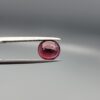 Studio close-up photographs displaying a 3.13-carat oval-cut natural rhodolite garnet gemstone featuring a unique surface inclusion detail on the front, held securely in precision tweezers against a neutral grey background.