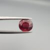 Studio close-up photographs displaying a 3.13-carat oval-cut natural rhodolite garnet gemstone featuring a unique surface inclusion detail on the front, held securely in precision tweezers against a neutral grey background.