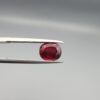 Studio close-up photographs displaying a 2.72-carat oval-cut natural rhodolite garnet gemstone held securely in precision tweezers against a neutral grey background.