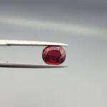 Studio close-up photographs displaying a 2.72-carat oval-cut natural rhodolite garnet gemstone held securely in precision tweezers against a neutral grey background.