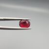 Studio close-up photographs displaying a 2.72-carat oval-cut natural rhodolite garnet gemstone held securely in precision tweezers against a neutral grey background.