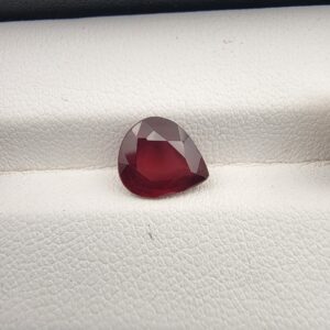Studio close-up photograph displaying a 2.81-carat pear-cut natural rhodolite garnet gemstone resting on a white textured display surface.