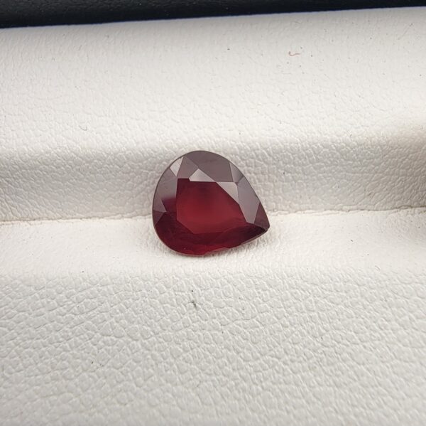Studio close-up photograph displaying a 2.81-carat pear-cut natural rhodolite garnet gemstone resting on a white textured display surface.