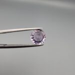 Studio close-up photographs displaying a 1.48-carat diamond-style cut natural amethyst Katela gemstone held securely in precision tweezers against a neutral grey background.