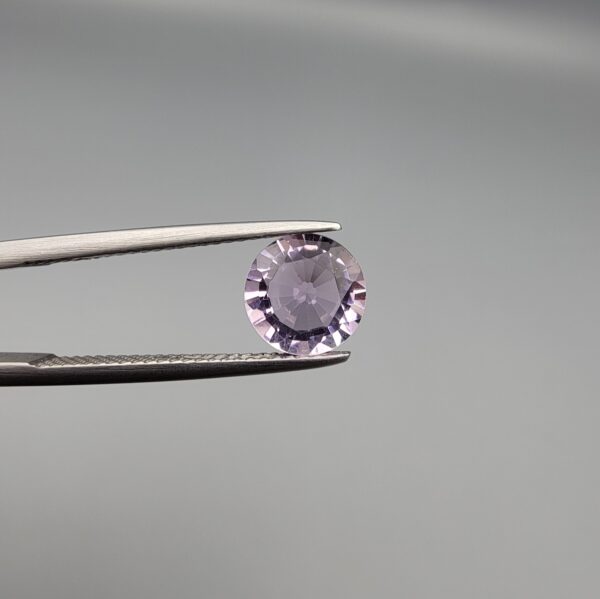 Studio close-up photographs displaying a 1.48-carat diamond-style cut natural amethyst Katela gemstone held securely in precision tweezers against a neutral grey background.