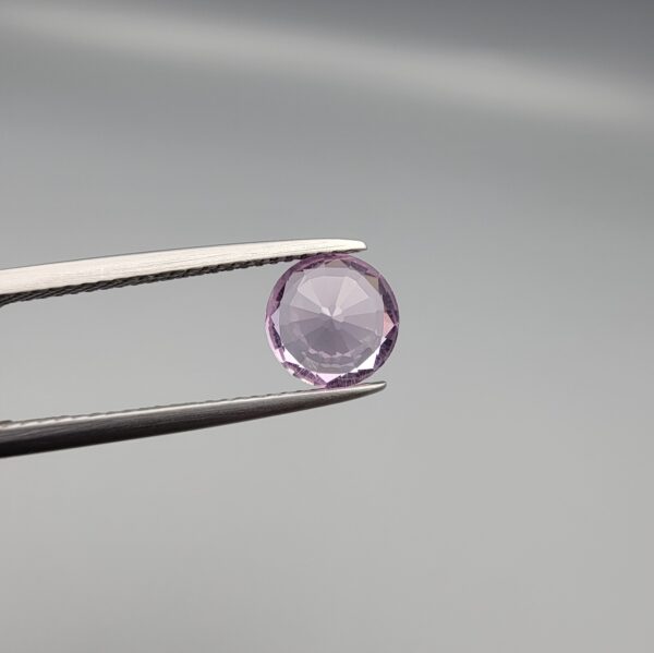 Studio close-up photographs displaying a 1.48-carat diamond-style cut natural amethyst Katela gemstone held securely in precision tweezers against a neutral grey background.