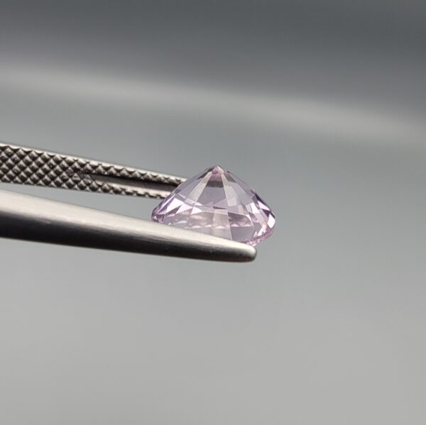 Studio close-up photographs displaying a 1.48-carat diamond-style cut natural amethyst Katela gemstone held securely in precision tweezers against a neutral grey background.