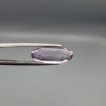 ​Studio close-up photographs displaying a 4.38-carat elongated oval-cut natural amethyst Katela gemstone held securely in precision tweezers against a neutral grey background.