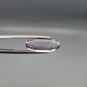 ​Studio close-up photographs displaying a 4.38-carat elongated oval-cut natural amethyst Katela gemstone held securely in precision tweezers against a neutral grey background.
