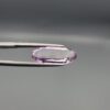​Studio close-up photographs displaying a 4.38-carat elongated oval-cut natural amethyst Katela gemstone held securely in precision tweezers against a neutral grey background.