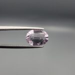 Studio close-up photograph displaying a 1.92-carat oval-cut natural amethyst Katela gemstone held securely in precision tweezers against a neutral grey background.