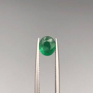 Studio close-up photograph showcasing an oval-cut 1.60 carat natural green emerald gemstone held securely in precision tweezers.