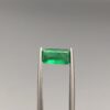 Studio close-up photographs showing the top-down view of an elongated rectangular step-cut 1.21 carat natural green emerald gemstone held securely in precision tweezers.