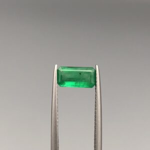 Studio close-up photographs showing the top-down view of an elongated rectangular step-cut 1.21 carat natural green emerald gemstone held securely in precision tweezers.