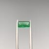 Studio close-up photographs showing the top-down view of an elongated rectangular step-cut 1.21 carat natural green emerald gemstone held securely in precision tweezers.