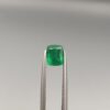 Studio close-up photograph showcasing a cushion-cut 1.18 carat natural green emerald gemstone held securely in precision tweezers.