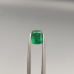 Studio close-up photograph showcasing a cushion-cut 1.18 carat natural green emerald gemstone held securely in precision tweezers.
