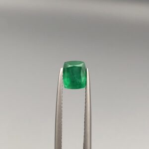 Studio close-up photograph showcasing a cushion-cut 1.18 carat natural green emerald gemstone held securely in precision tweezers.