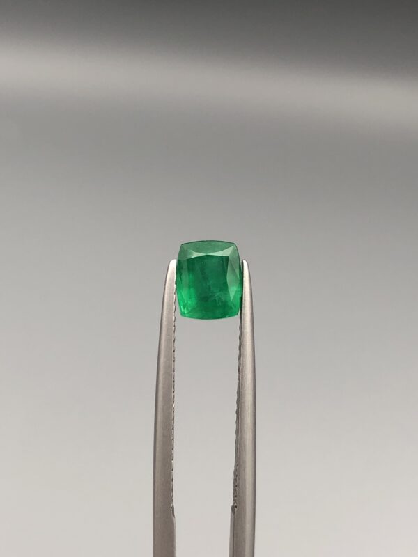 Studio close-up photograph showcasing a cushion-cut 1.18 carat natural green emerald gemstone held securely in precision tweezers.
